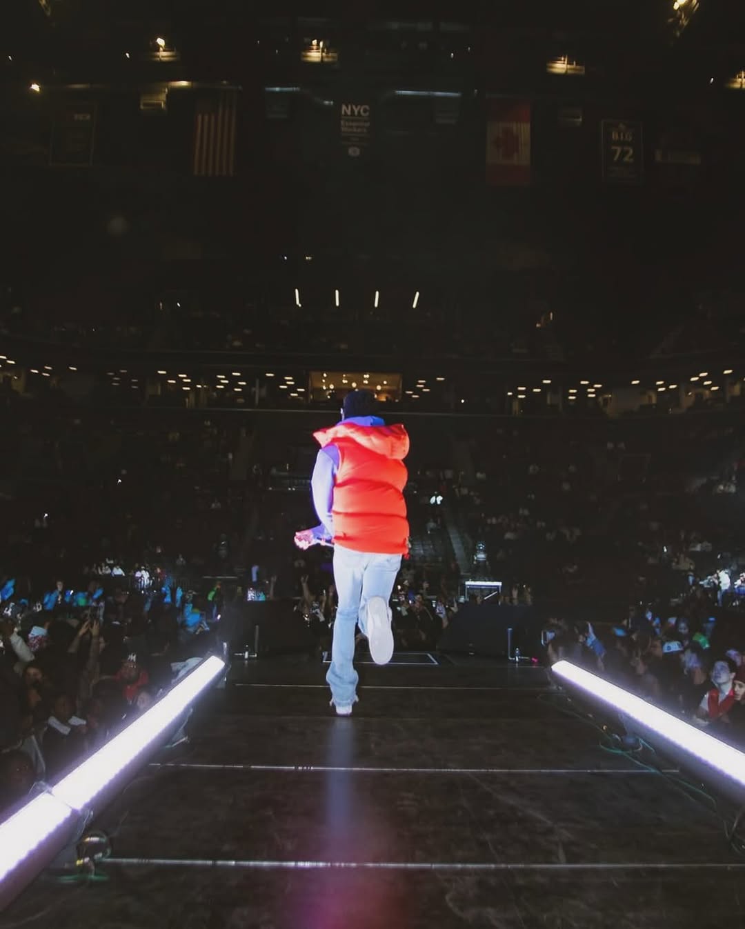 CJ WestCoast walking down a lit stage runway toward a massive arena