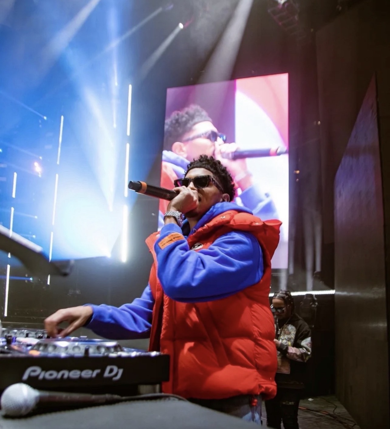 CJ WestCoast on the decks with a microphone, performing under stage lights
